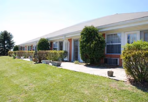 Single-story senior living facility with a lawn, hedges, and front entrances along a walkway.