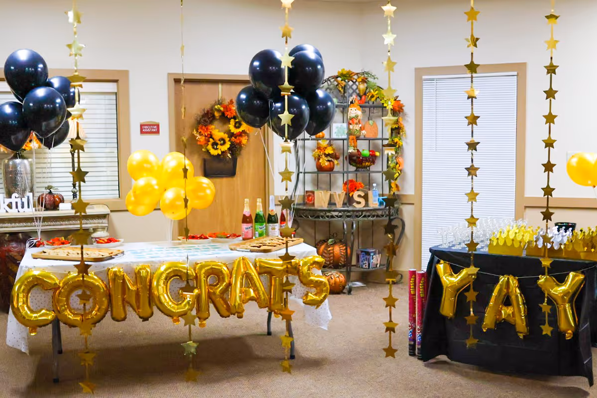 Indoor celebration setup at Tallgrass Healthcare Campus with gold CONGRATS balloons, a YAY display, star garlands, and tables of snacks.