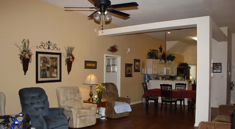 Open-plan living and dining area with several recliner chairs, a ceiling fan, and a dining table by the kitchen counter.
