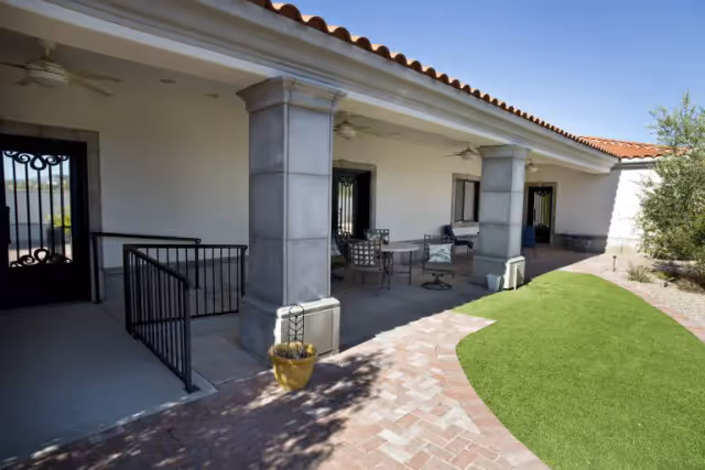 Covered outdoor patio with stone columns, metal doors and seating beside a brick walkway and small lawn.
