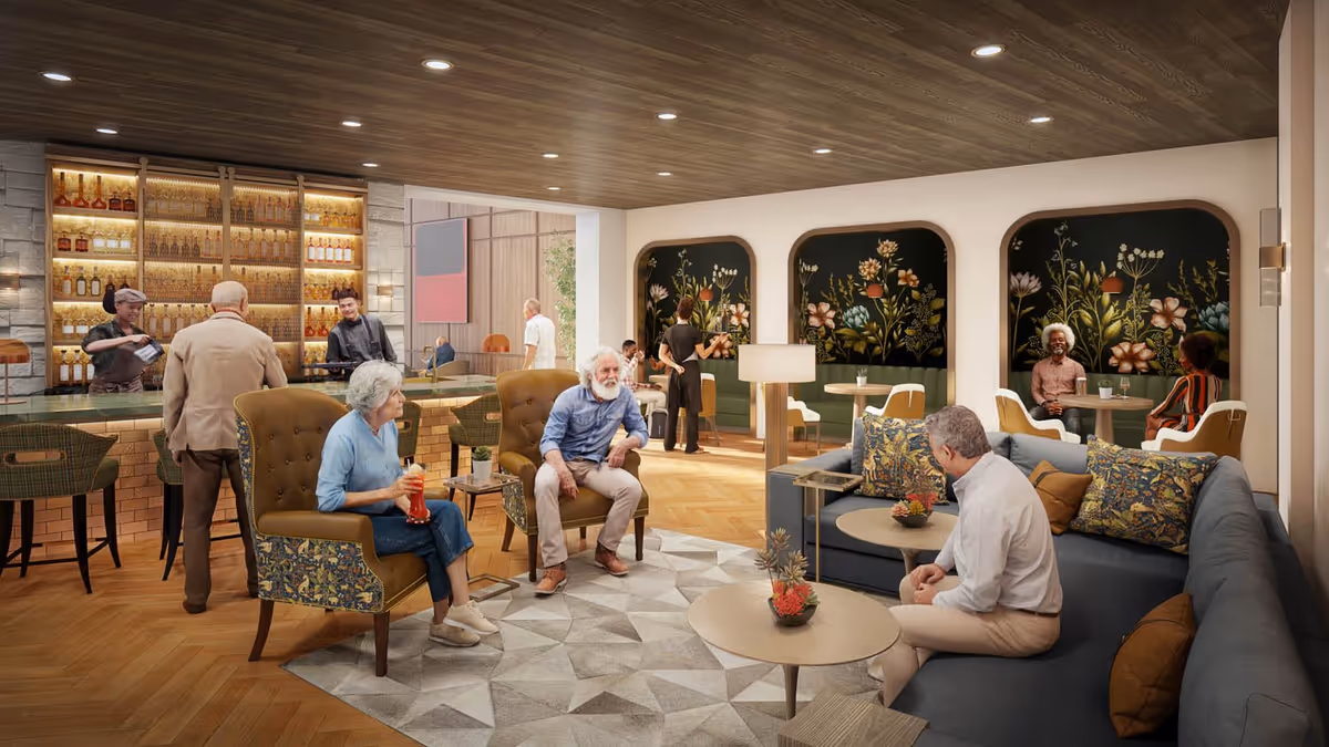 A cozy lounge area in a senior living facility featuring a bar with two bartenders serving drinks. Several elderly people are seated on comfortable chairs and sofas, engaging in conversation. The room has a wooden ceiling with recessed lighting, a patterned rug, and floral artwork on the walls behind booth seating areas.