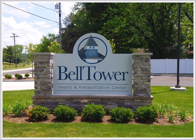 Outdoor stone and sign structure displaying the name 'BellTower Health & Rehabilitation Center' with a logo of a bell tower above the text, surrounded by green grass, shrubs, and trees in the background.