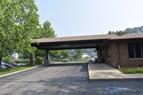 Front exterior of Caring Place facility with brick building, carport, and handicapped parking.