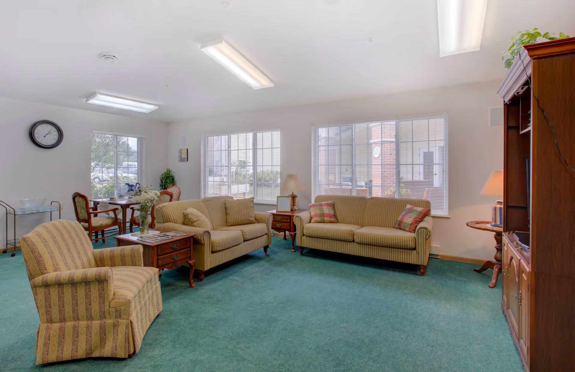 A bright communal living room with sofas, armchairs, side tables and large windows.