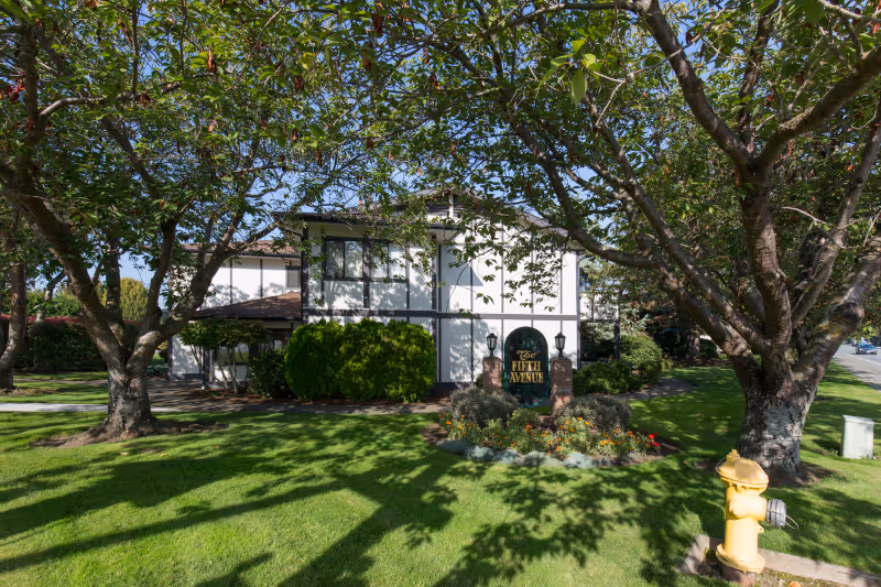 Front exterior of a two-story building with a green lawn, trees, flowerbed and a sign reading 'Fifth Avenue'.