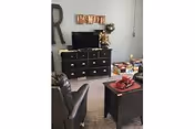A cozy living room area with a black leather armchair, a black dresser with a television on top, and a small black coffee table with decorative items. The wall behind the dresser has a large letter 'R' and a decorative sign that says 'FAMILY'. There are various board games stacked on the floor near the dresser.