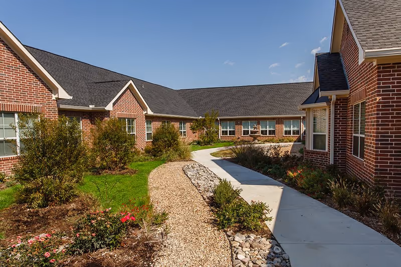 The Westmore Senior Living campus exterior with curved walkway and landscaped garden beds.