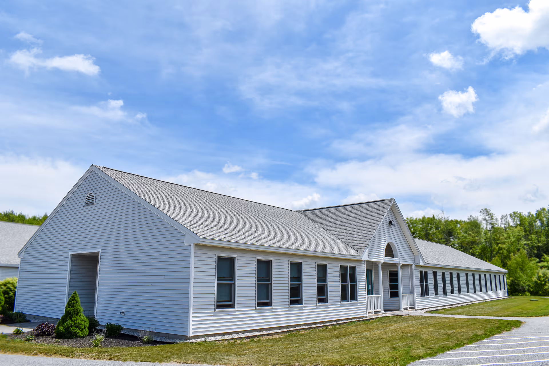 Long single-story white siding building with multiple windows and a covered entrance under a blue sky.