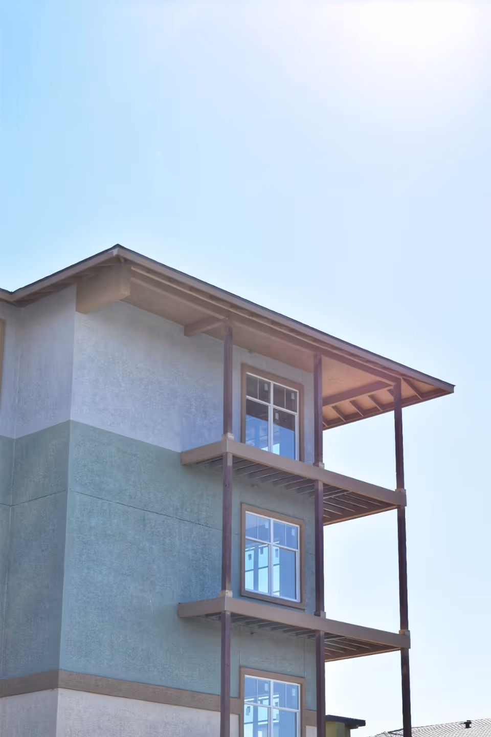 Exterior view of a three-story building facade with stacked balconies and windows against a clear blue sky.
