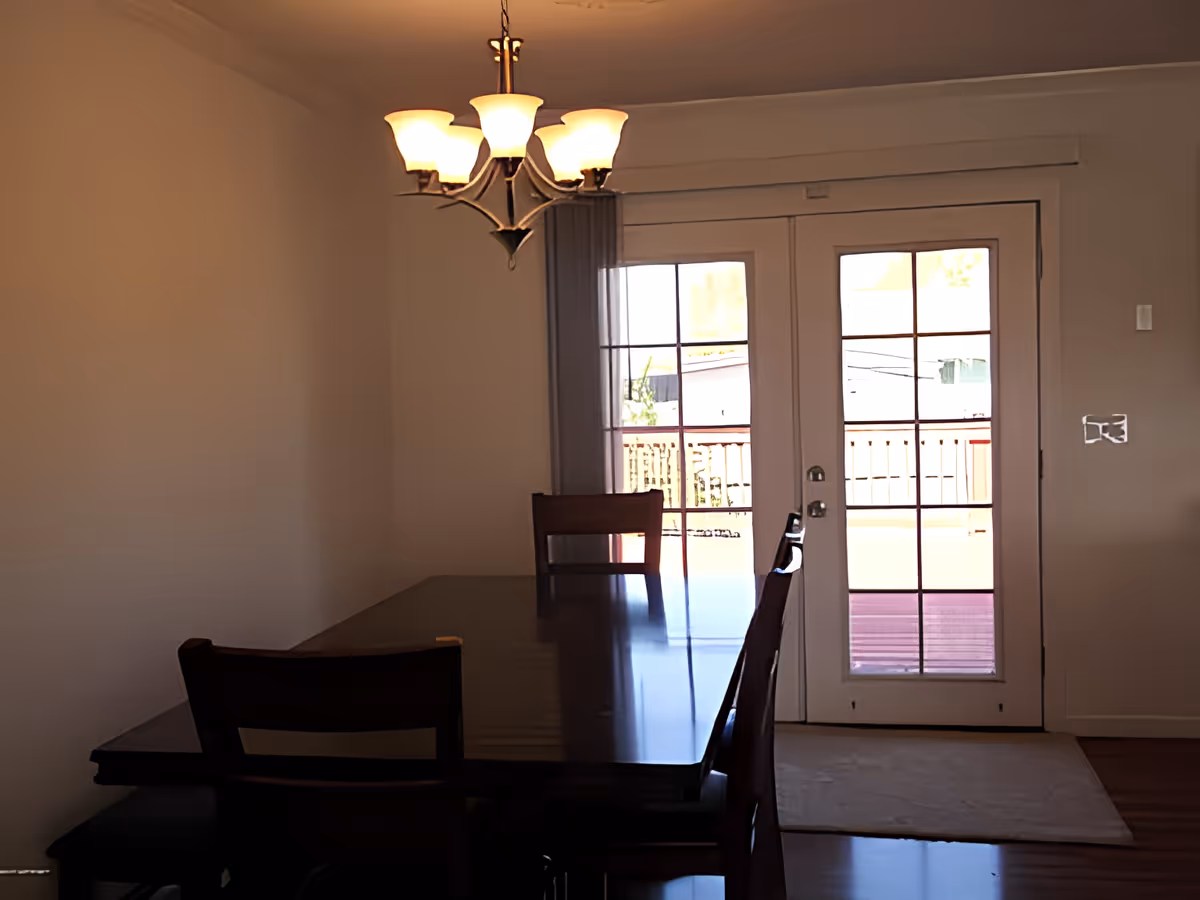 Dining room with a dark wooden table and chairs under a chandelier and French doors leading outside.