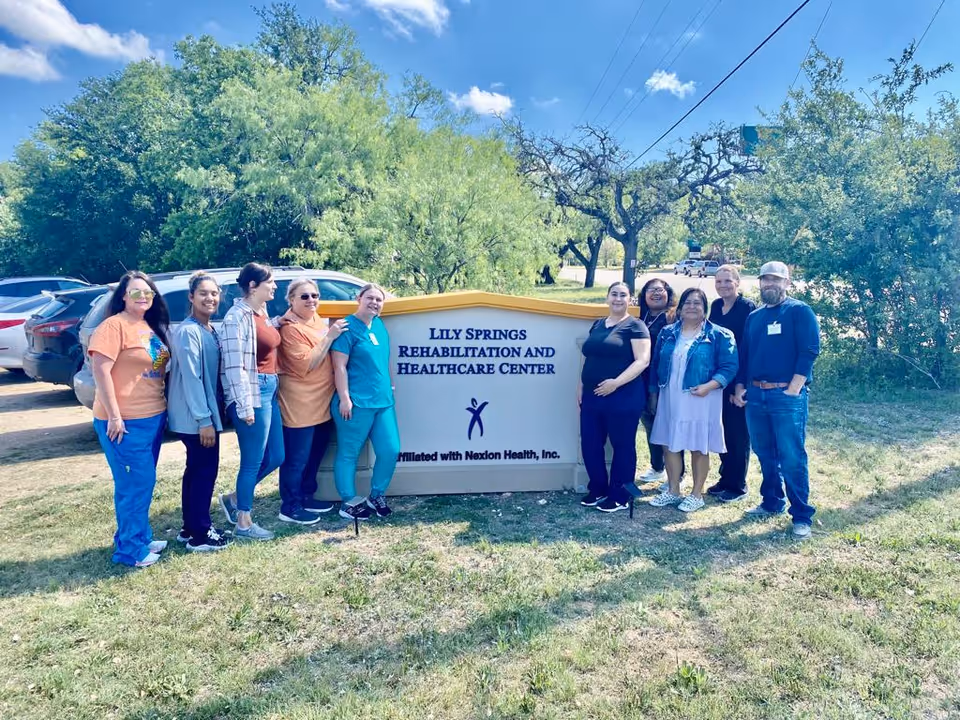 A group of staff standing outdoors around a sign reading "Lily Springs Rehabilitation and Healthcare Center."