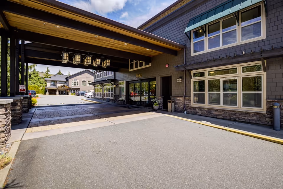 Covered porte-cochere and entrance driveway in front of a senior living building with stone accents and large windows.