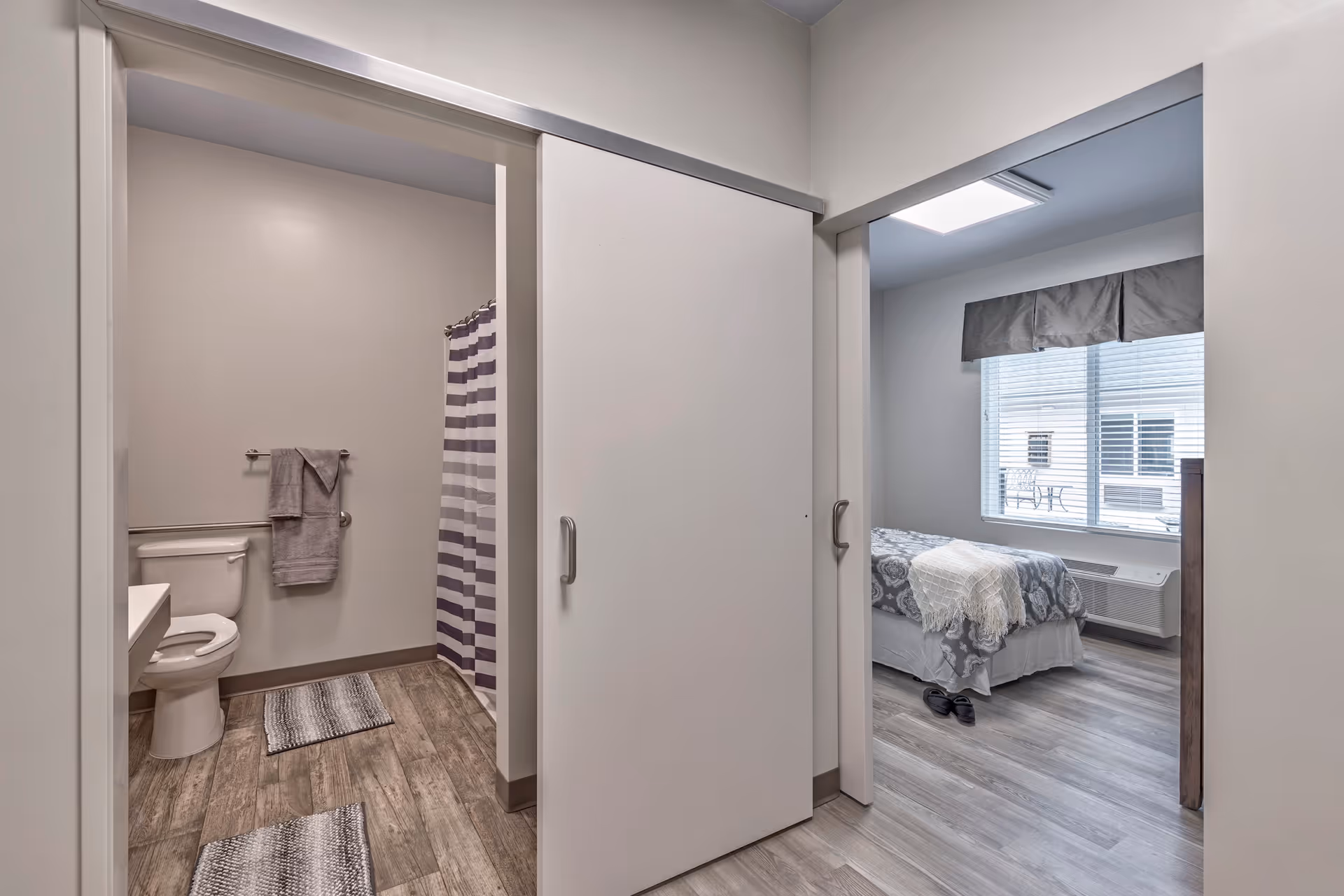 Interior view of a unit showing a bathroom with shower and toilet on the left and a bedroom with a bed on the right separated by sliding doors.