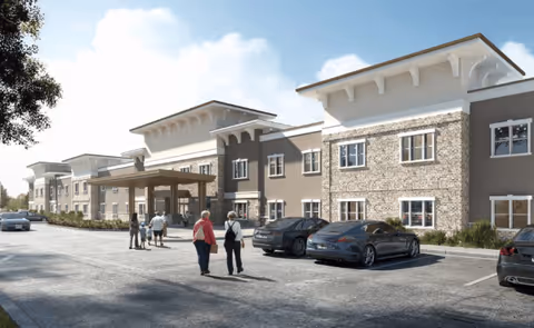 Exterior view of a modern senior living facility building with a covered entrance. Several people are walking towards the entrance, and multiple cars are parked in front of the building under a clear blue sky.
