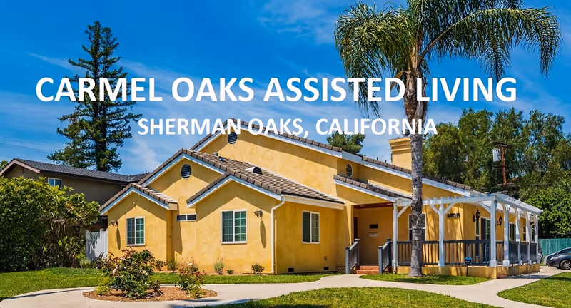 Exterior view of Carmel Oaks Assisted Living facility in Sherman Oaks, California, showing a yellow building with a tiled roof, a porch with white railings, palm trees, and a well-maintained lawn under a blue sky.