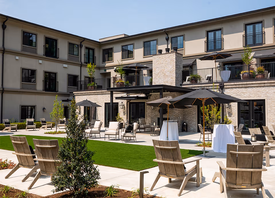 Outdoor courtyard of a multi-story senior living building with lounge chairs, umbrellas, tables, and balconies.
