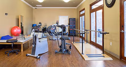 Interior rehab gym featuring exercise equipment and parallel bars.