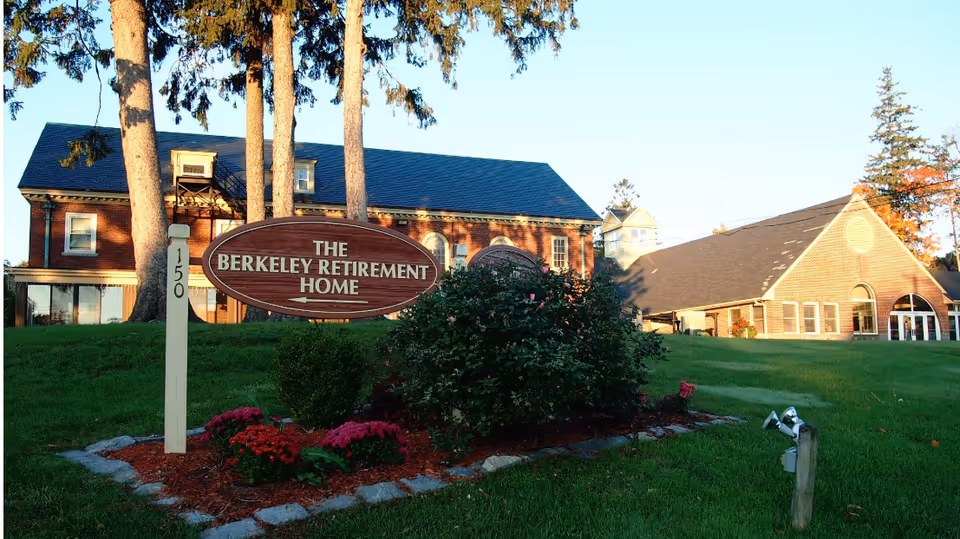 Front lawn and wooden sign reading "The Berkeley Retirement Home" with brick buildings in the background.
