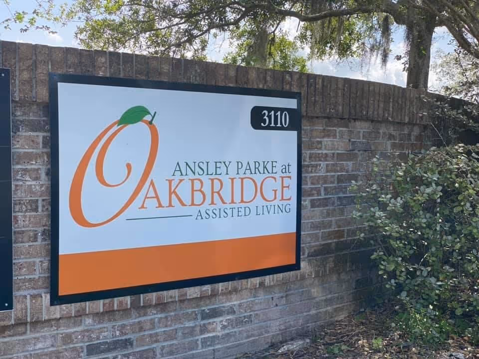 Entrance sign mounted on a brick wall reading "Ansley Parke at Oakbridge Assisted Living" with the number 3110 and nearby shrubs.