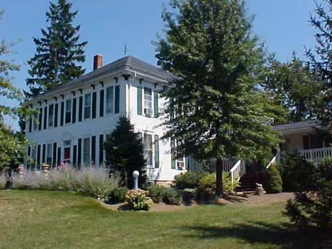 White two-story building with many windows, surrounded by trees and a manicured lawn.