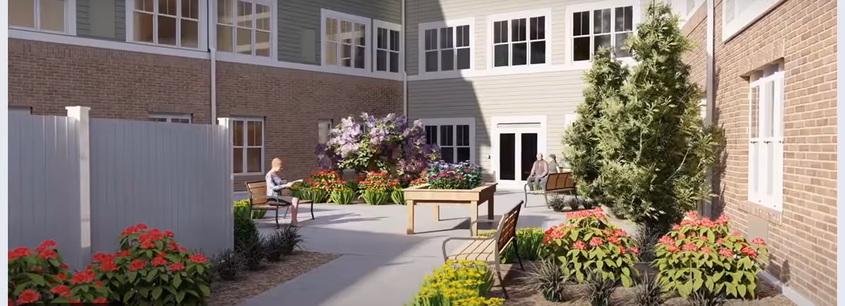Sunlit courtyard with benches, raised planters, colorful flowers and a few seated residents beside a multi-story senior living building.