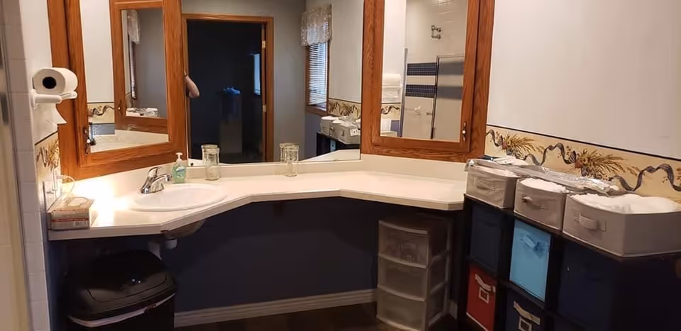 Corner bathroom vanity with a sink, large mirrors, soap dispenser and organized storage bins.