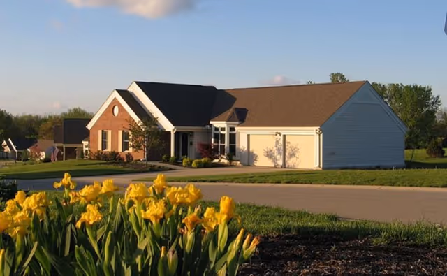 Single-story suburban building with an attached garage and a bed of yellow flowers in the foreground.