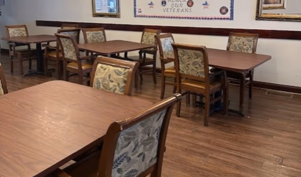 Dining room with wooden tables and patterned chairs in a senior living facility.