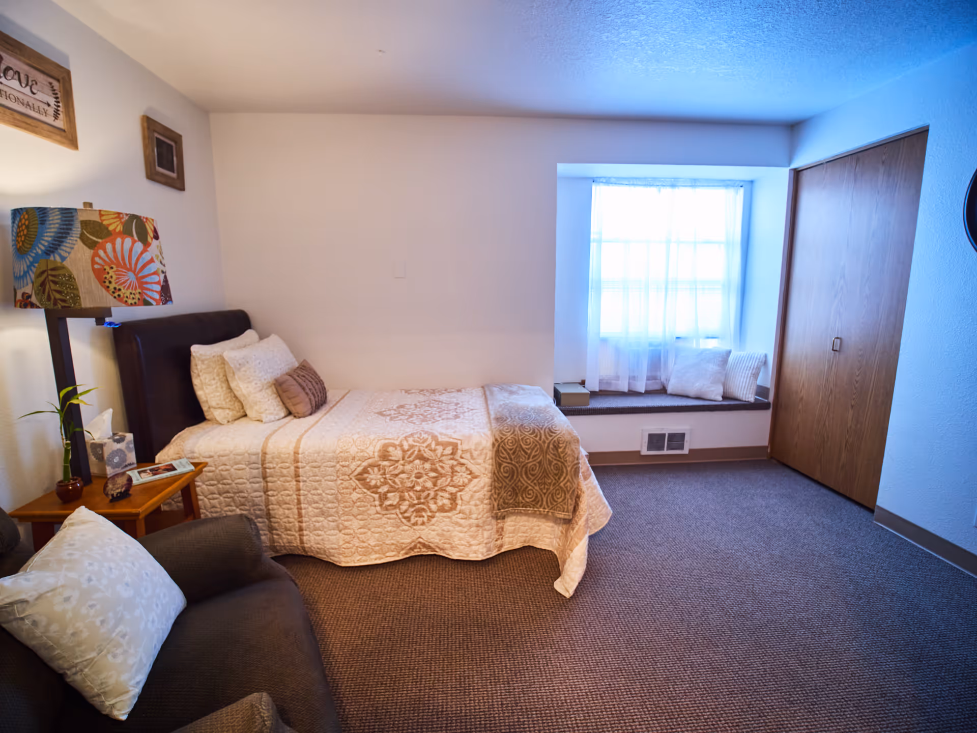 A cozy bedroom with a single bed, bedside table and armchair next to a window seat and closet.