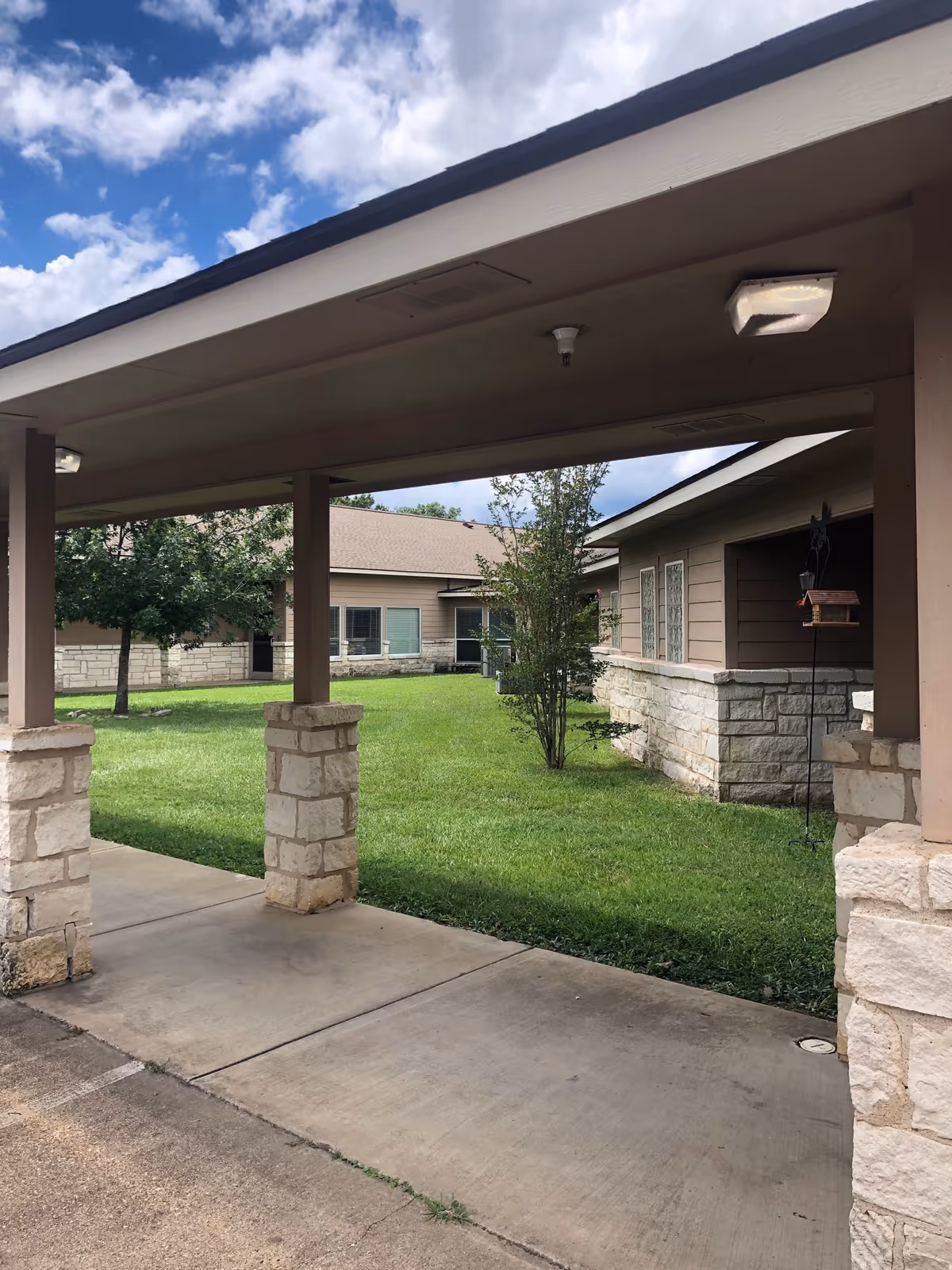 A view of a senior living facility's entrance, featuring a covered walkway and green lawn.