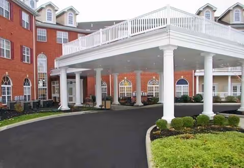 Brick senior living facility exterior with a white portico, columns, and landscaped entrance.