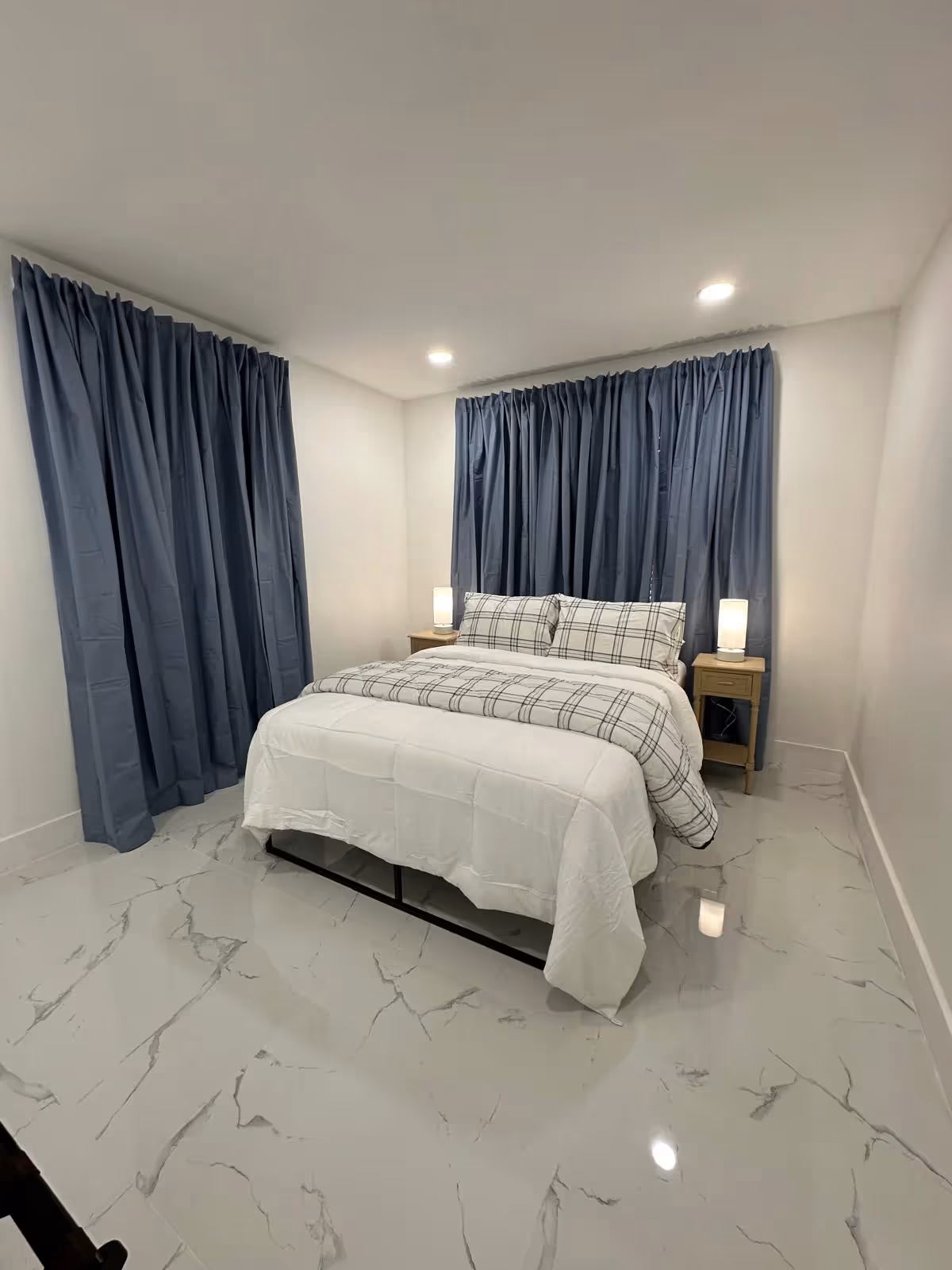 A neatly made bedroom with a bed, two nightstands with lamps, and blue curtains.