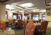 Well-lit dining room with multiple tables set for service and floral-upholstered chairs under a coffered ceiling.