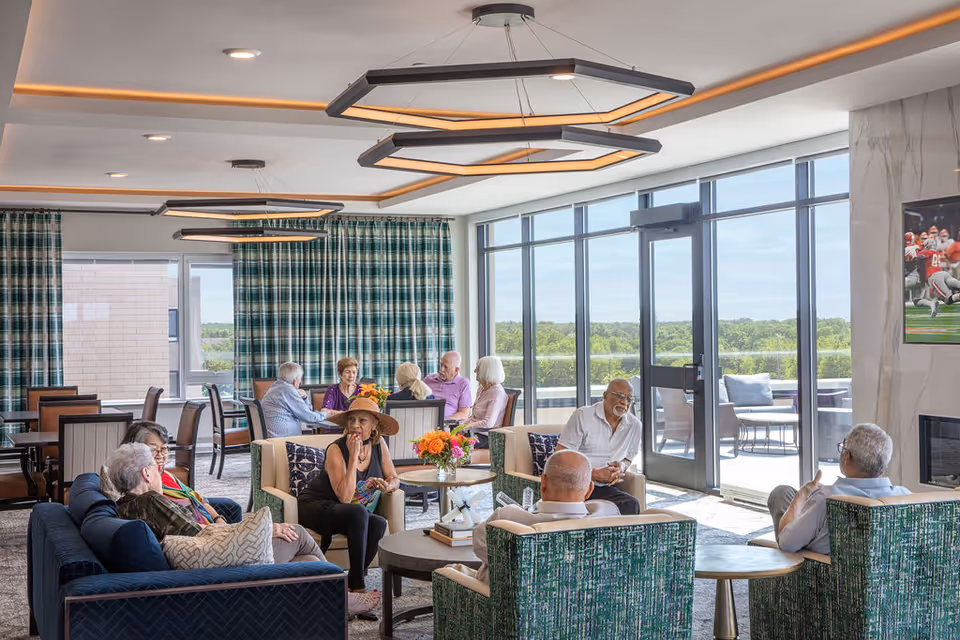 Sunny communal lounge with sofas, armchairs, modern lighting and large windows where several people are socializing.