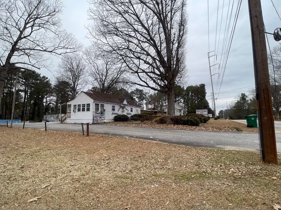 A single-story white building on a roadside lot with leafless trees and a grassy foreground.
