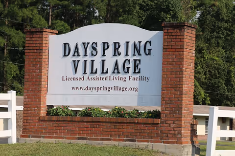 Brick entrance sign reading "Dayspring Village, Licensed Assisted Living Facility" with landscaping and trees behind.