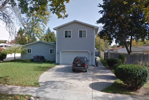 Two-story gray senior living facility with driveway, attached garage, and parked car.