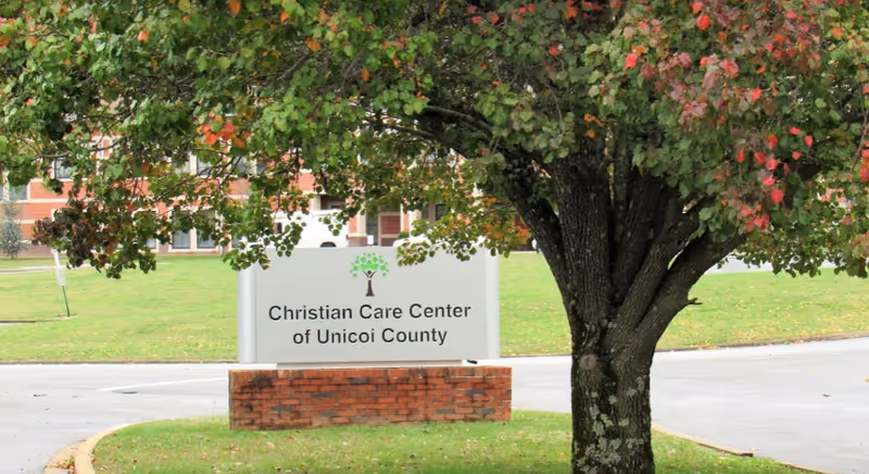 Entrance sign reading 'Christian Care Center of Unicoi County' in front of a tree with the facility building and lawn visible behind it.