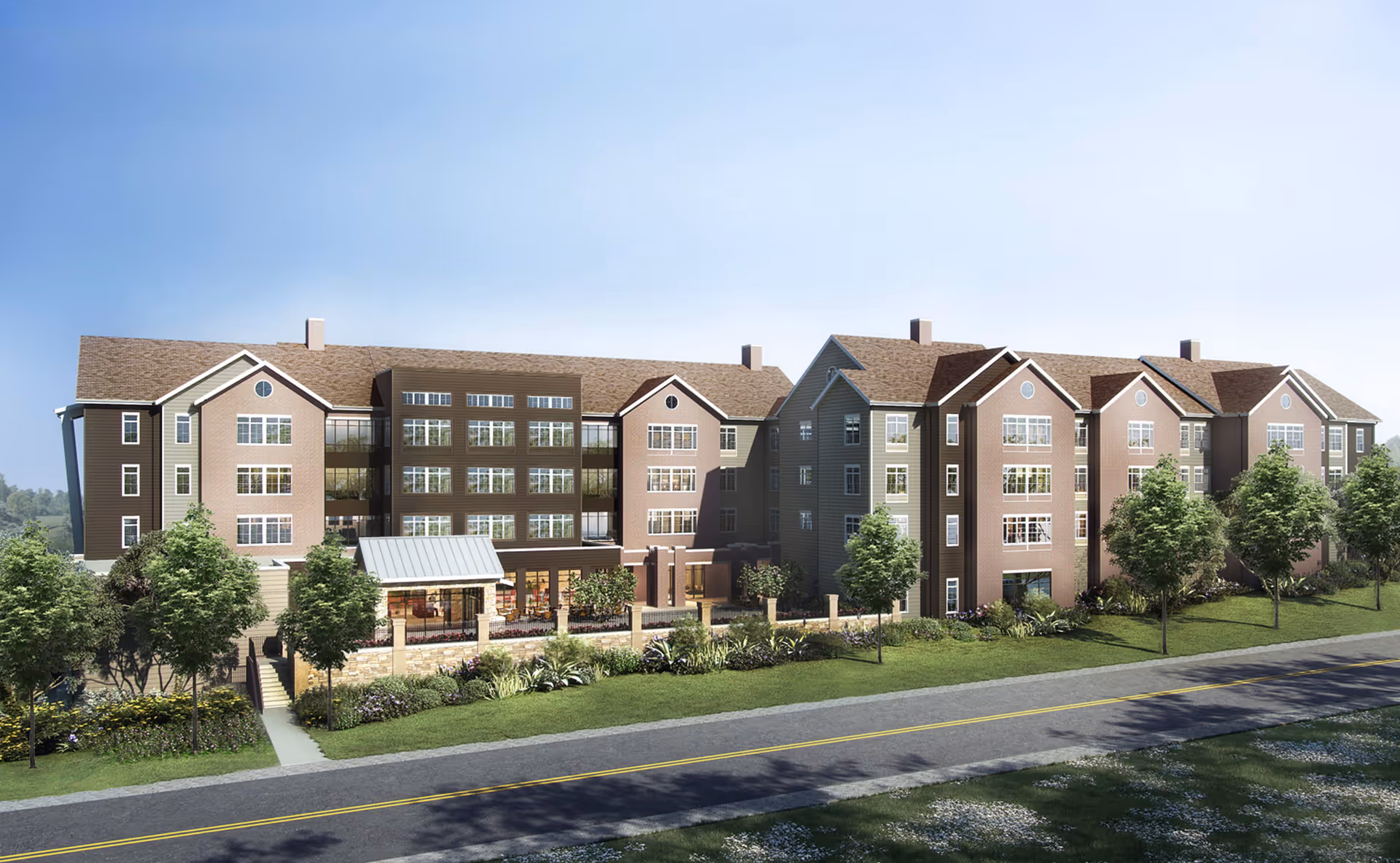 Exterior view of a large, multi-story senior living facility building with multiple windows, pitched roofs, and a landscaped front yard with trees and shrubs under a clear blue sky.