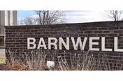 Brick entrance wall with large white letters spelling "BARNWELL" and dried shrubs in front against a partly cloudy sky.