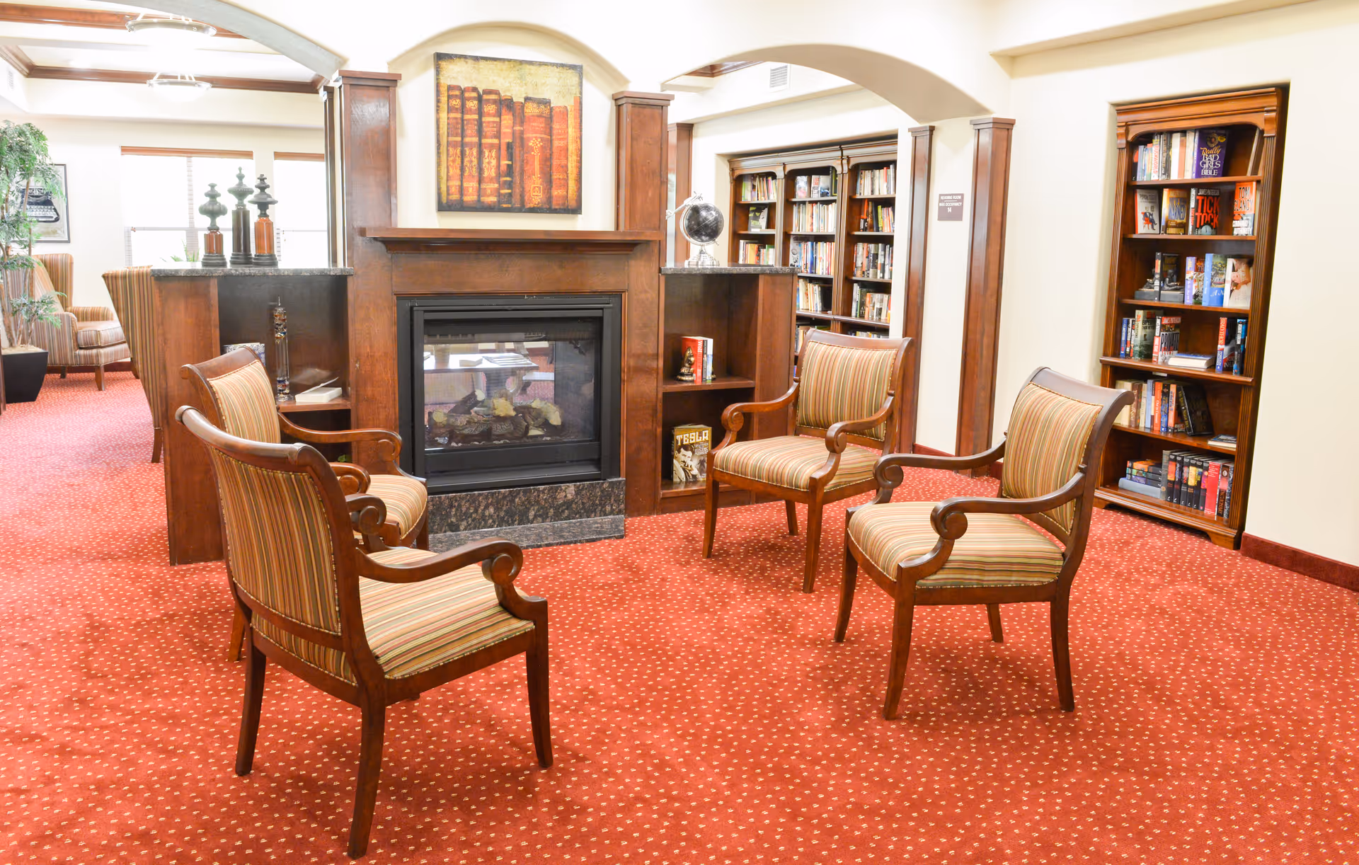 Cozy lounge area with four striped armchairs arranged around a fireplace and bookshelves.