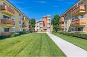 Symmetrical senior living complex with beige buildings, orange balconies, central walkway, and manicured lawn.