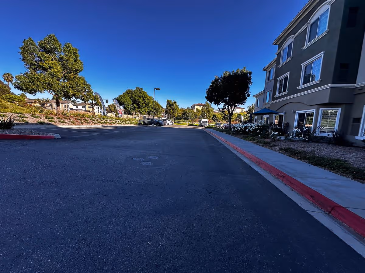 Driveway and landscaped entrance area in front of a multi-story residential building with trees under a clear blue sky.