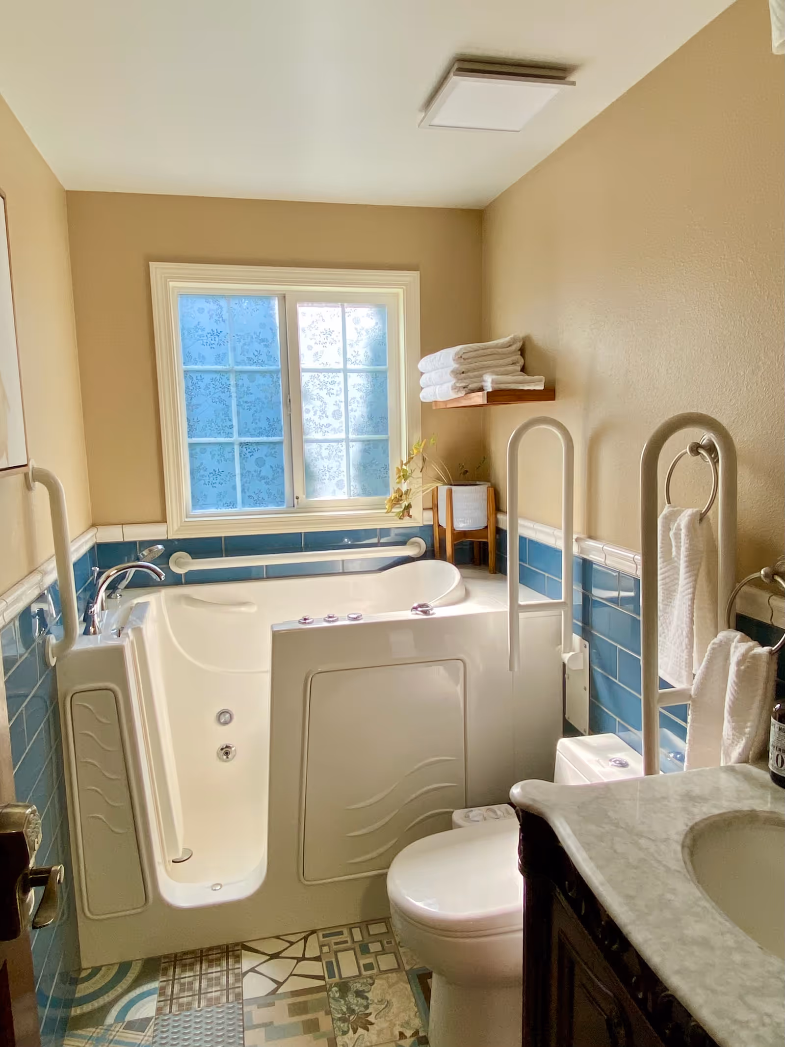 Well-lit bathroom with a walk-in tub, grab bars, toilet, sink, and a window with frosted patterned glass.