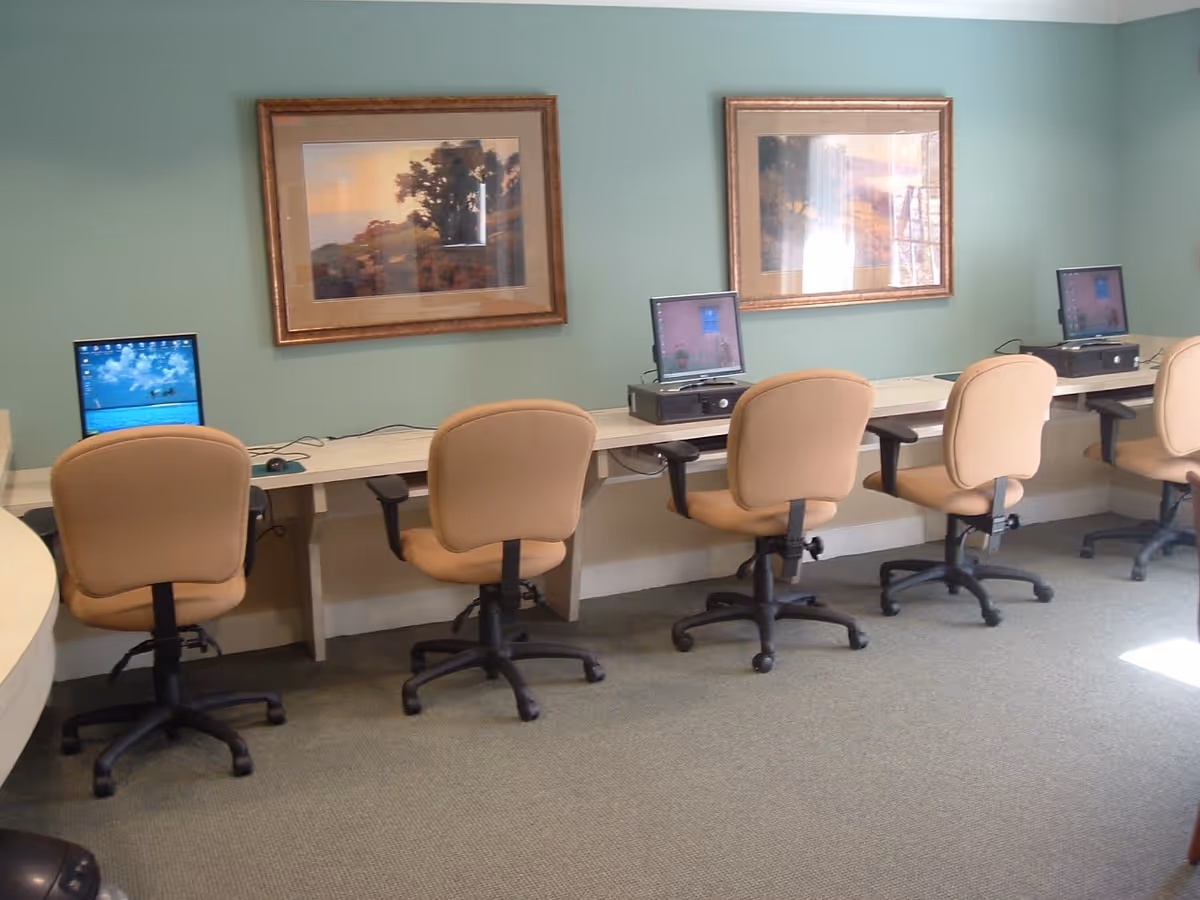Row of computer workstations with beige swivel chairs and framed artwork on a light green wall.