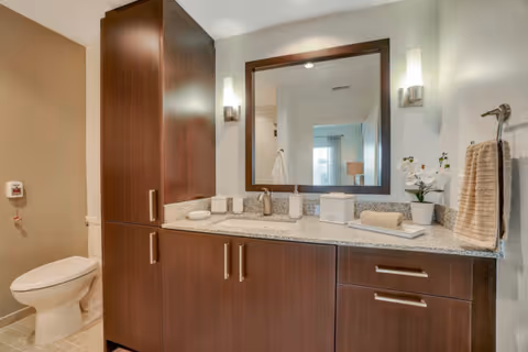 Modern bathroom with a dark wood vanity, granite countertop, mirror, sink, and a toilet.
