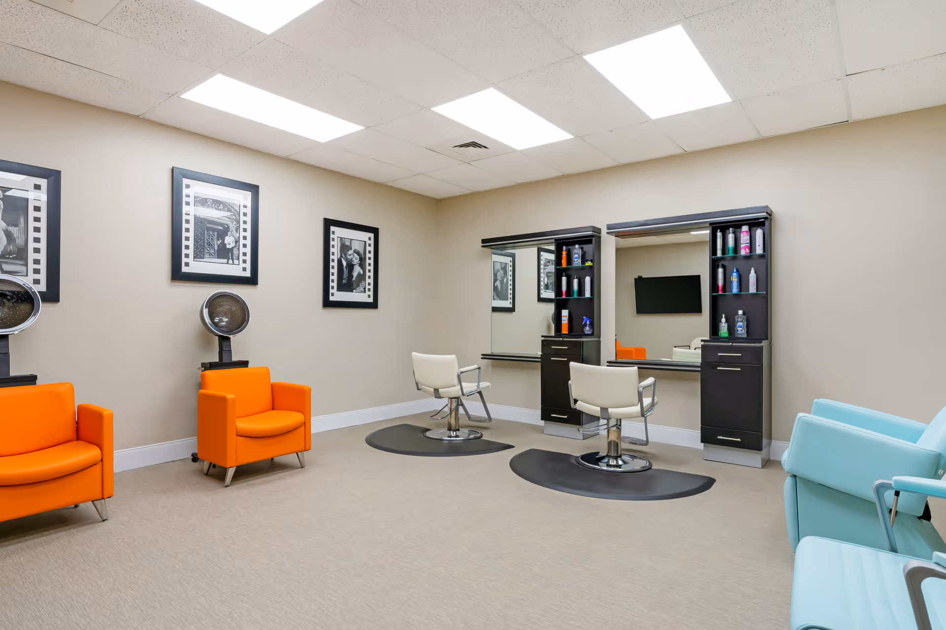 Interior salon room with two styling stations, mirrors and chairs, shelves of hair products and colorful waiting chairs.