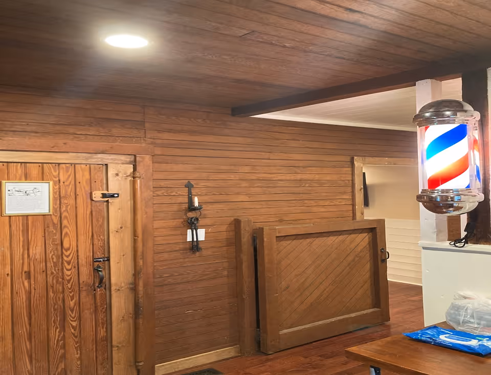 Wood-paneled interior space with a closed wooden door, a waist-high half-door, a mounted barber pole light, and a small table in the corner.