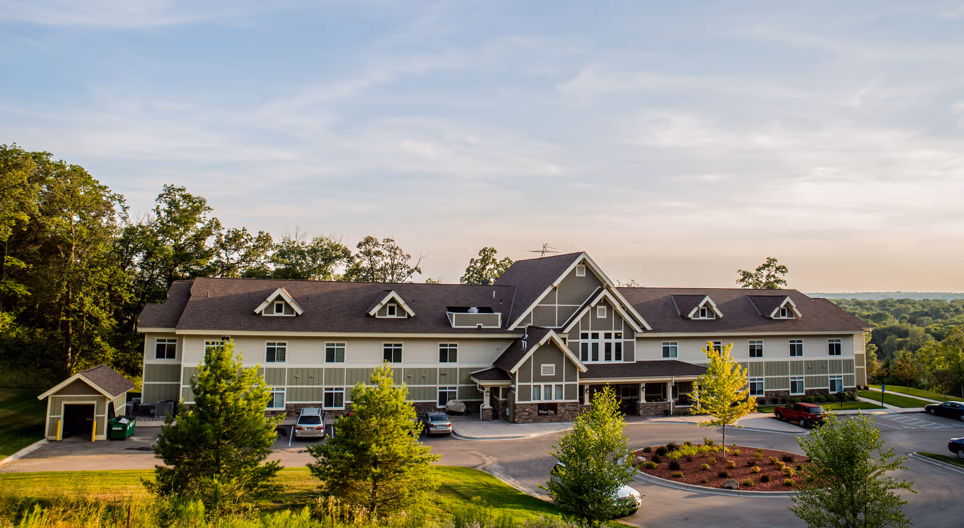 Exterior view of a large memory care facility with parking and landscaped grounds.