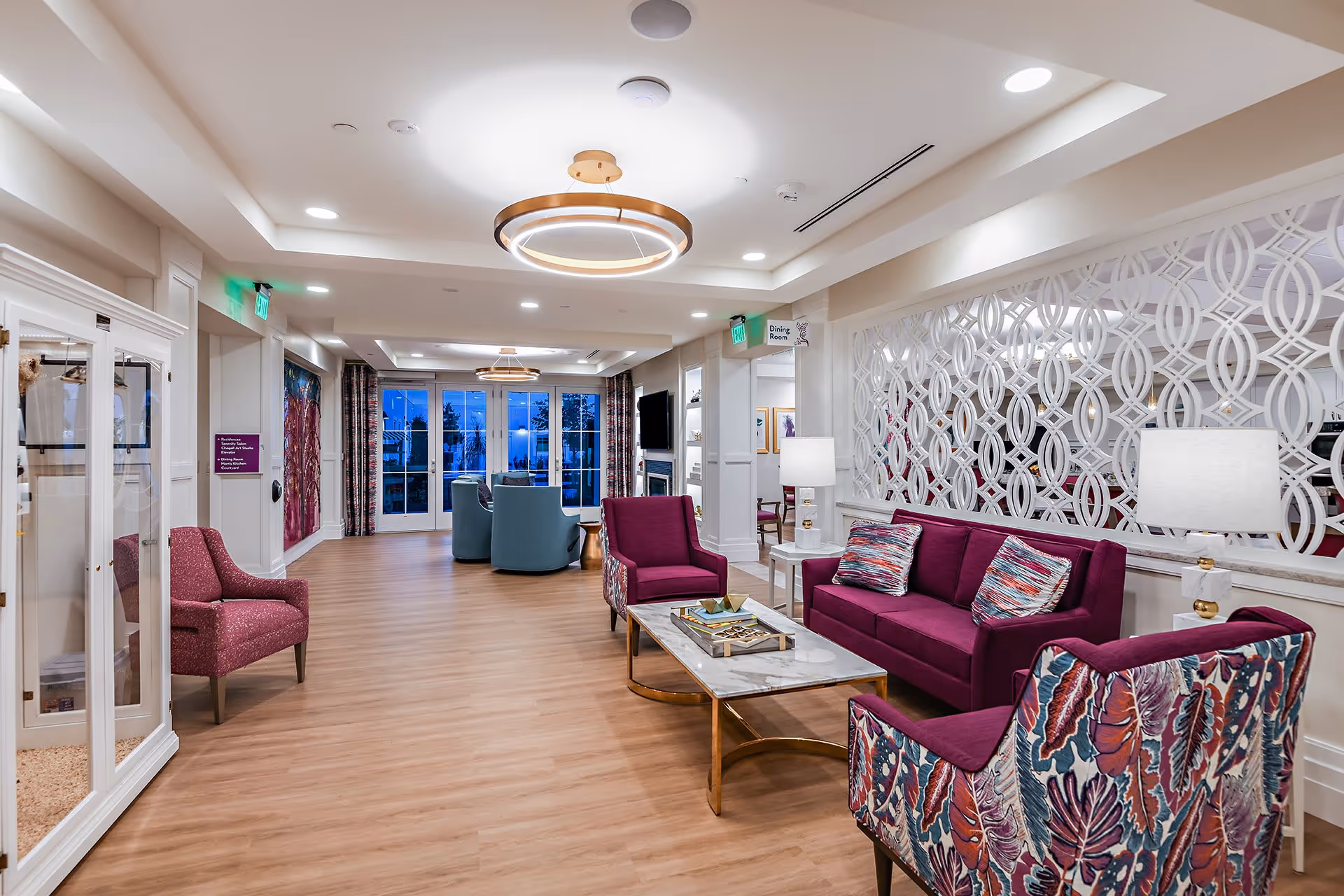 Spacious, bright communal lounge with purple sofas and patterned chairs arranged around a coffee table.